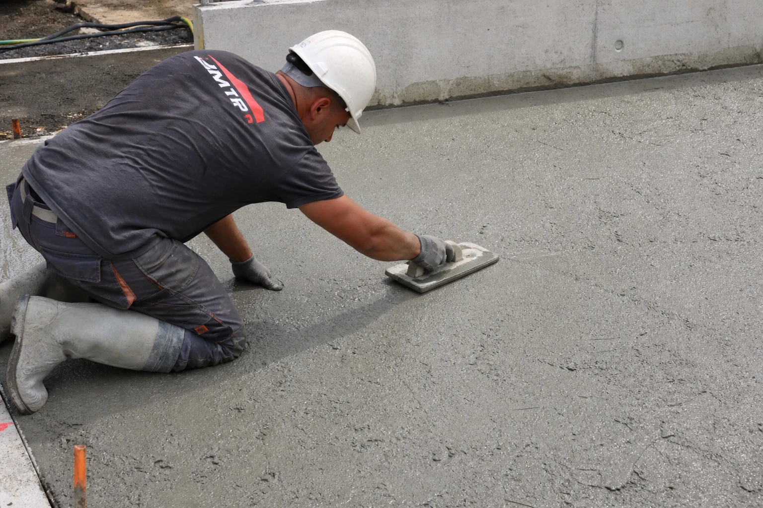 Ouvrier lissant une dalle de béton fibré fraîchement coulée sur un chantier extérieur